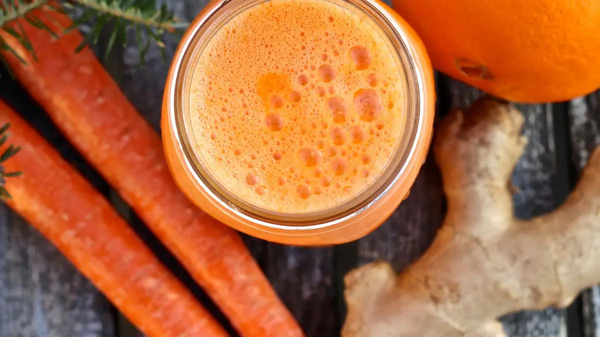 Suco detox de cenoura, laranja, pepino e gengibre servido em copo alto com gelo.